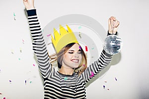 Young smiling woman on white background celebrating party, wearing stripped dress and yellow paper crown, happy dynamic