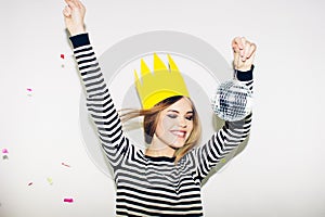 Young smiling woman on white background celebrating party, wearing stripped dress and yellow paper crown, happy dynamic