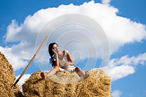 Young smiling woman in white dress sitting on hay stack