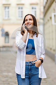 Young smiling woman in white shirt walking through the streets of old europe city and talking on the phone