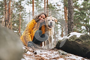 Young smiling woman in yellow jacket with big kind white dog Labrador walking in the winter forest