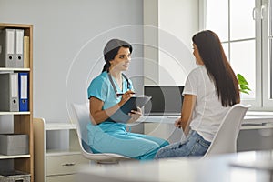 Young smiling doctor listening to woman patients complaints and making notes in medical clinic photo