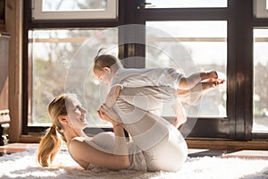 Young smiling yogi mother and her baby daughter exercising toget