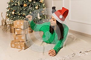 The young smilling girl lying near Christmas festive tree and brown gifts