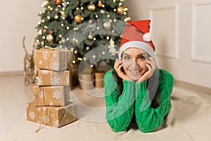 The young smilling girl lying near Christmas festive tree and brown gifts