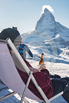 Young snowboarder cheering with a beer after skiing day in a bar or a cafe at the Zermatt ski resort