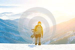 Mladý snowboardista lezúci na horu s doskou v ruke v zlatej hodine