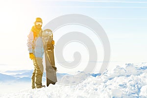 Mladý snowboardista v helmě stojící vedle snowboardu strčený do sněhu se sluncem za zády