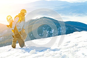 Young snowboarder in helmet walking at the top of a mountain at sun-set