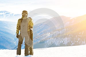 Mladý snowboardista stojící vedle snowboardu vraženého do sněhu ve zlaté hodině
