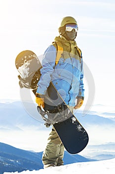 Mladý snowboardista so slnkom za ním sa chystá vyliezť na horu