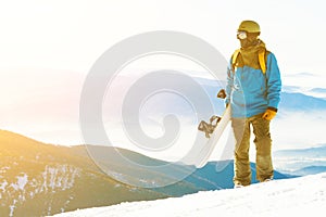 Young snowboarder with sun behind him looking at a landscape from the top of a mountain