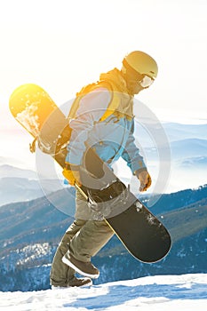 Young snowboarder walking at the top of a mountain with sun behind him