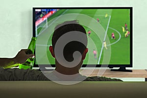 Young soccer fan man watching European football game on big screen television at living room sofa couch enjoying and feeling