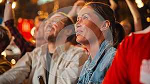 Young Soccer Fans Couple Watching a Live Football Match in a Sports Bar. Crowd with Colored Faces