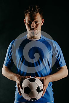Young soccer player with ball on black background in studio.