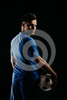 Young soccer player with ball on black background in studio.