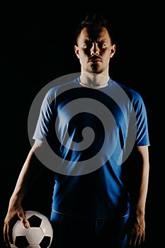 Young soccer player with ball on black background in studio.