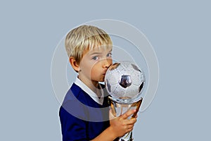 Young soccer player in blue jersey holds winners cup after the goal, isolated at light background