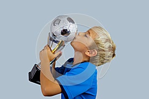 Young soccer player in blue jersey holds winners cup after the goal, isolated at light background