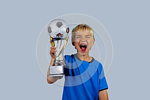 Young soccer player in blue jersey holds winners cup after the goal, isolated at light background