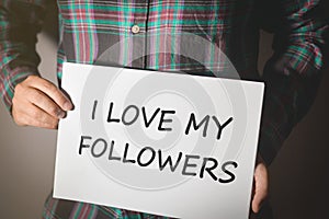 Young social media influencer in plaid shirt holding a placard with text: I LOVE MY FOLLOWERS!