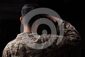 Young soldier saluting standing on black background