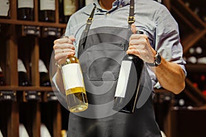 Young sommelier holding bottle of red wine in cellar