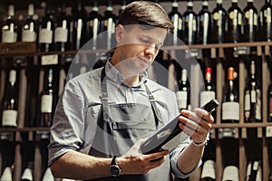 Young sommelier holding bottle of red wine in cellar