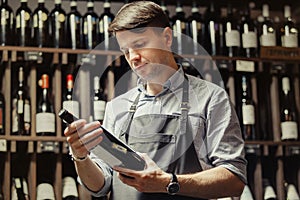 Young sommelier holding bottle of red wine in cellar