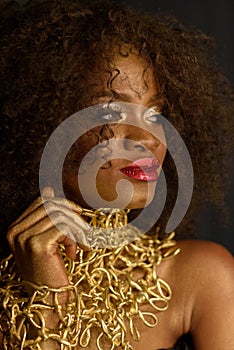 Young South African woman in gold makeup and accessories with a pensive, but sly expression
