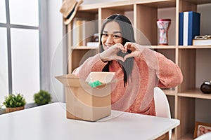 Young south asian woman opening cardboard box smiling in love doing heart symbol shape with hands