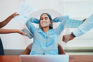 Young South Asian woman relaxes in office chair while coworkers make demands