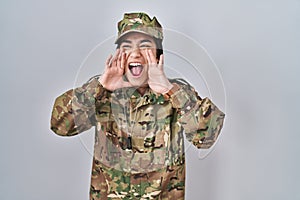 Young south asian woman wearing camouflage army uniform shouting angry out loud with hands over mouth