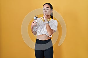 Young south asian woman wearing sportswear drinking water looking confident at the camera smiling with crossed arms and hand