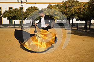 Young Spanish man in black shirt, jacket and pants, with dancing shoes, dancing flamenco with black and gold capote in the street photo