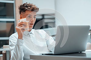Young Spanish man holding cash Euro and working on a computer