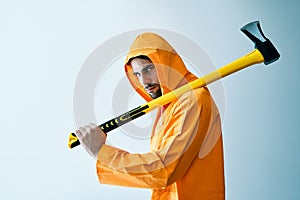 Young spooky man in orange raincoat holding big axe