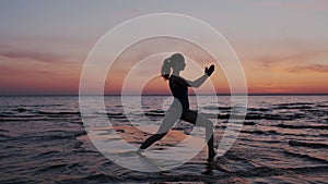 Young sport and flex woman exercising yoga, doing warrior pose on beach during sundown sky. silhouette of a slim and fit