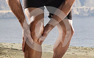 Young sport man with athletic legs holding knee in pain suffering muscle injury running photo