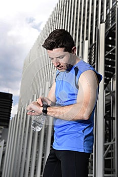 Young sport man checking time on chrono timer runners watch holding water bottle after training session