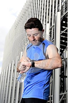 Young sport man checking time on chrono timer runners watch holding water bottle after training session photo