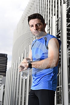 Young sport man checking time on chrono timer runners watch holding water bottle after training session photo