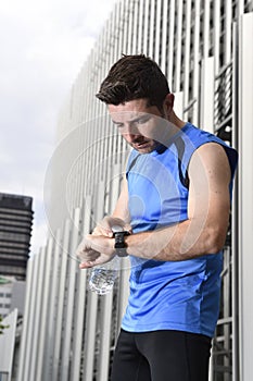 Young sport man checking time on chrono timer runners watch holding water bottle after training session photo