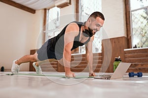Young sport man doing up push ups exercise in empty gym or home watching online sports videos. Muscular sportsman doing