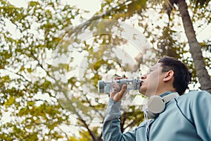 Young sport man drink water after jogging, running in the park. Sport thirsty and resting after exercise