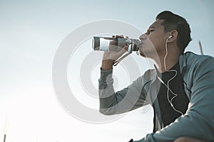 Young sport man drink water after jogging, running in the park. Sport thirsty and resting after exercise