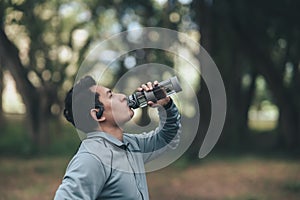 Young sport man drink water after jogging, running in the park. Sport thirsty and resting after exercise