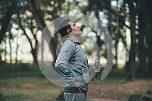 Young sport man drink water after jogging, running in the park. Sport thirsty and resting after exercise