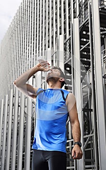 Young sport man drinking water bottle after running training session in business district